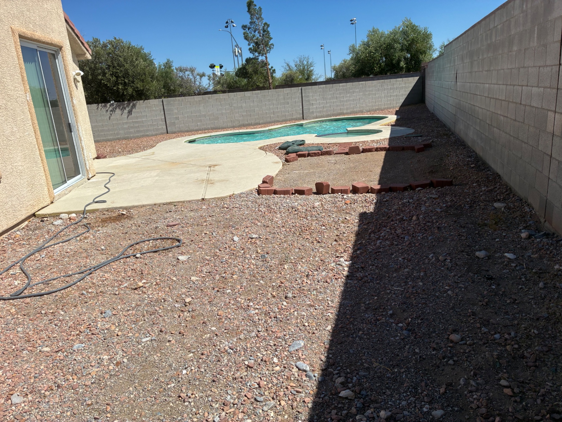 Pool and spa with overgrown dry weeds in the surrounding rock beds