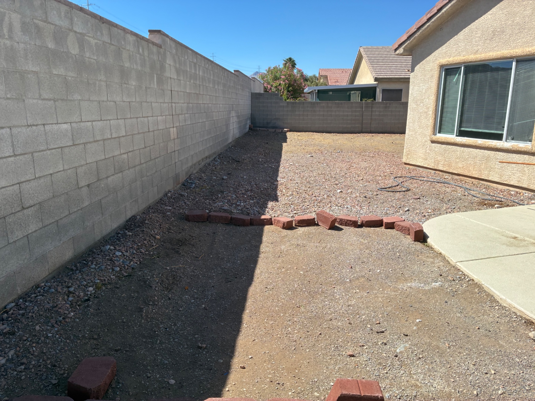 Long dirt side yard along the house with red bricks set as a temporary barrier